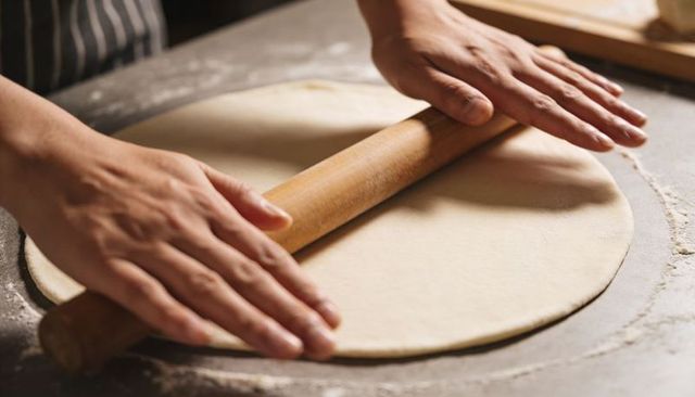 Rolling dough with wooden pin on floured countertop for handmade pizza and pastry