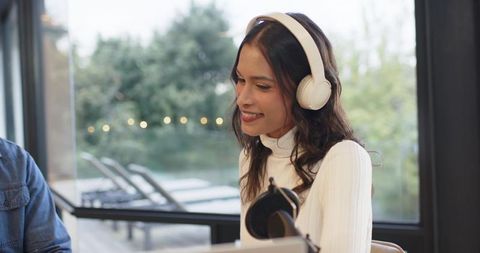 Smiling woman recording podcast with headphones in modern glass-walled coworking studio