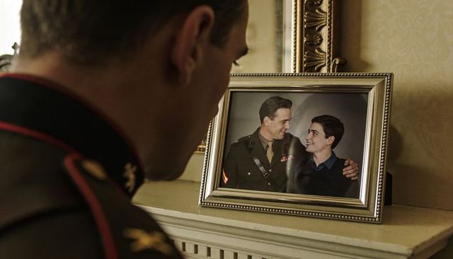 Soldier reflecting at mantel while gazing at framed military portrait of mentor