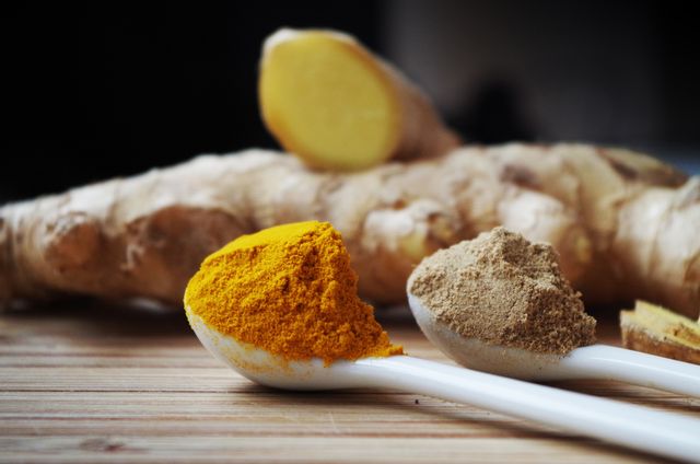 This image shows fresh ginger root with spoonfuls of turmeric and ginger powder on a wooden surface, highlighting natural and organic ingredients. It can be used in cooking websites, health blogs, culinary workshops, and marketing materials for organic food products to stress the importance of healthy and natural remedies.