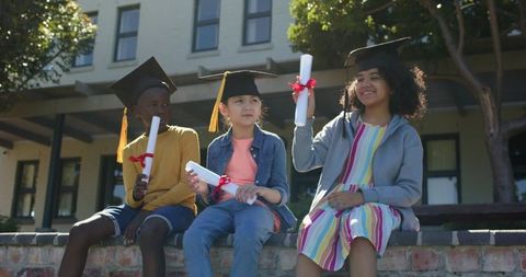 Young graduates celebrating on sunlit campus wearing mortarboards holding diploma scrolls
