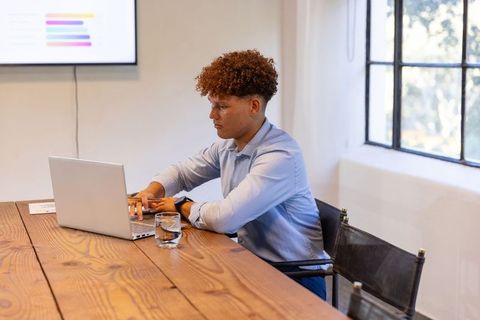 Young professional working on laptop in modern meeting room with bar chart display