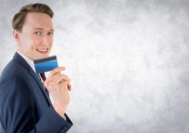 Businessman in a suit holding a credit card and smiling against a white grunge background. Ideal for use in financial services, banking, corporate presentations, payment solutions, and business-related marketing materials.