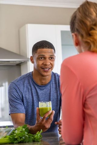 African american man and woman sharing green smoothie, smiling at kitchen island