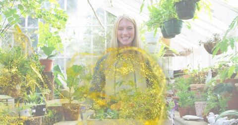 Smiling gardener tending seedlings in light-filled glasshouse with golden sparkles