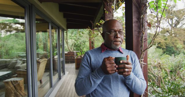 Elderly man stands on a deck, holding a coffee mug, enjoying a peaceful morning surrounded by nature. Ideal for conveying themes of relaxation, retirement, casual lifestyle, and tranquility. Perfect for use in retirement home promotions, health and wellness blogs, or advertisements targeting senior audiences.