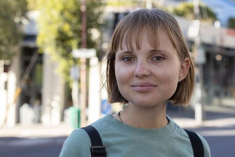 Confident young woman wearing nose ring and backpack posing on urban sidewalk in daylight