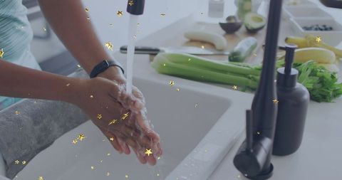 Washing hands at kitchen sink with lathered soap, black faucet, fresh produce on counter