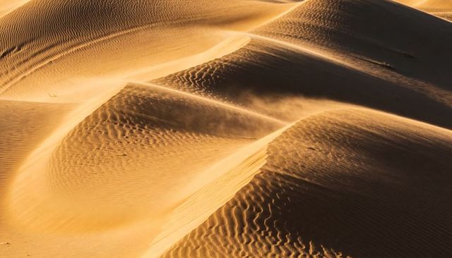Golden desert dunes shifting and revealing rippled sand patterns at sunrise