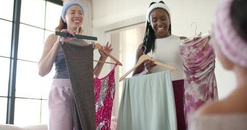 African american friends comparing dresses and trying on party outfits at home