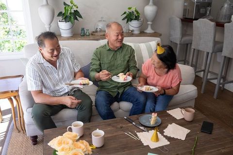 Asian family celebrating at home sharing cake with senior woman wearing party hat