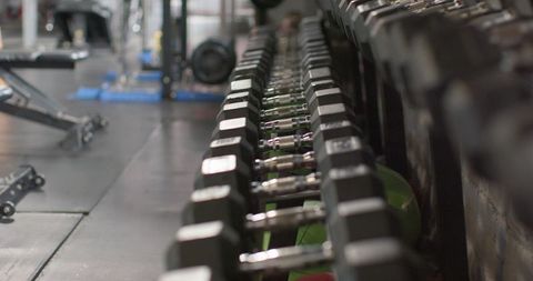 Row of hex dumbbells on rack with reflective steel handles in modern gym interior