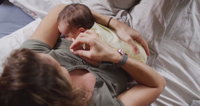 A mother is breastfeeding her newborn baby while lying on a bed. This intimate moment highlights maternal care and the natural bond between mother and child. The setting appears cozy and comfortable, emphasizing nurturing and love. This can be used in contexts related to motherhood, infant care, family bonding, breastfeeding support, and natural parenting.