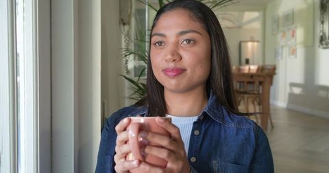 Woman enjoying quiet morning holding ceramic mug by sunlit window in cozy home