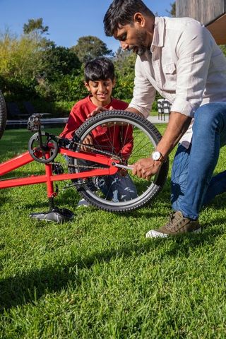 Father and son repairing bicycle together in sunny backyard