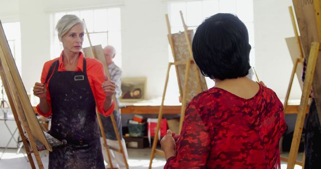 Mature artists engaged in a painting class, actively interacting and working on their pieces in an art studio filled with natural light. This visual can be used to represent art education, weekend hobbies, or community creative events.