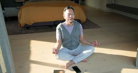 Asian Man Practicing Meditation on Sunlit Bedroom Floor