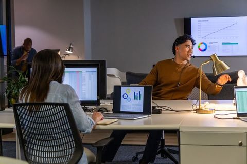 Asian man presenting to team in open-plan office with charts and laptops, collaboration