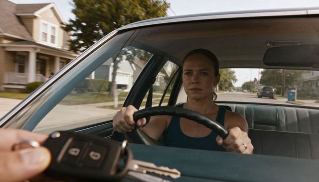 Serious woman driving gripping steering wheel while key fob held in foreground suburban street