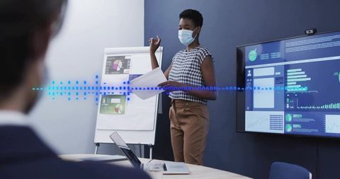 Masked presenter leading boardroom meeting with digital dashboards and data visualization