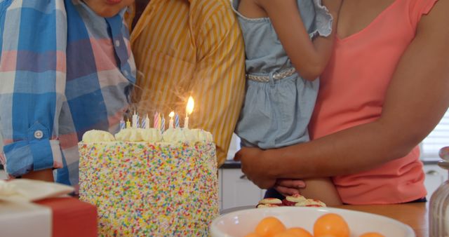 People celebrating a birthday around a table with a birthday cake filled with lit candles. Ideal for use in family celebration promotions, birthday greeting cards, and event planning websites.