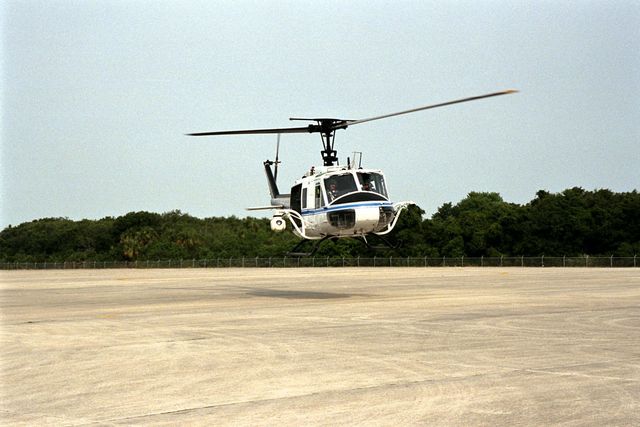 This image shows a NASA Huey UH-1 helicopter landing at the Shuttle Landing Facility at Kennedy Space Center, picking up security personnel equipped with Forward Looking Infrared Radar (FLIR) and portable GPS systems. This setup aids Florida's Division of Forestry in monitoring and combating brush fires. Ideal for depicting emergency response, forest firefighting, and advanced aviation technology.