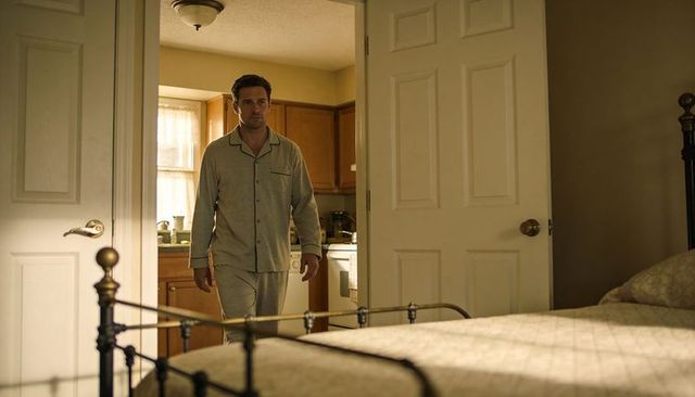 Man walking in gray pajamas through bedroom doorway toward kitchen morning routine