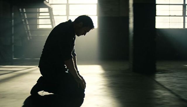 Kneeling man in sunlit warehouse showing solitude and reflection in dusty light