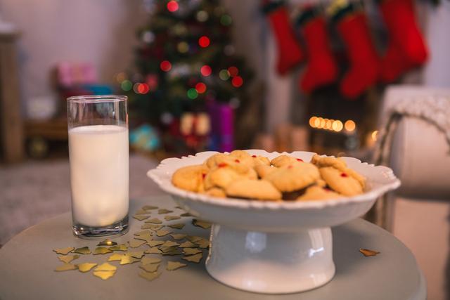 Christmas cookies with a glass of milk on a table near a decorated Christmas tree. The background features Christmas stockings and festive lights, creating a cozy holiday atmosphere. Perfect for themes of holiday celebrations, family gatherings, festive food preparations, and Christmas traditions.