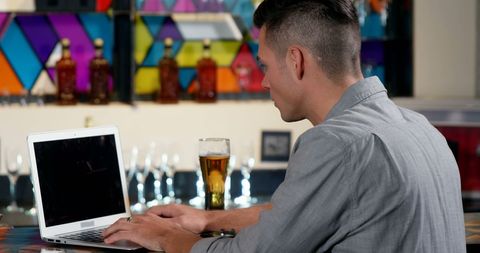 Man Working on Laptop with Beer in Trendy Bar