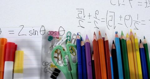 Displaying colorful study desk with colored pencils, scissors, clips and math scribbles for educatio