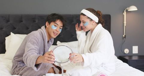 Couple enjoying at-home spa night applying under-eye patches on bed