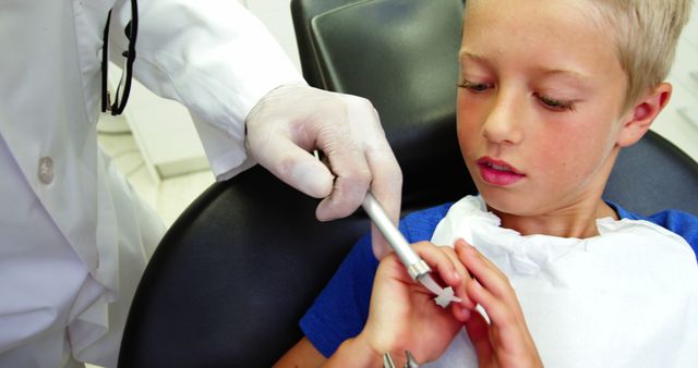 Young boy sitting in a dental chair while a dentist, wearing gloves, provides dental treatment. Ideal for use in medical websites, dental care brochures, or educational materials about children's health and dentistry.