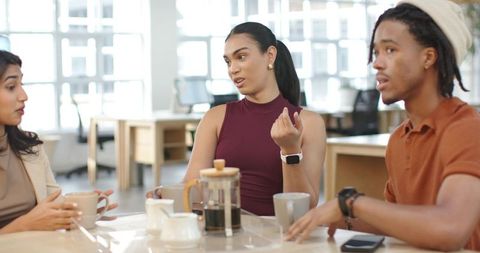 Young professionals discussing project over coffee in bright coworkorking space