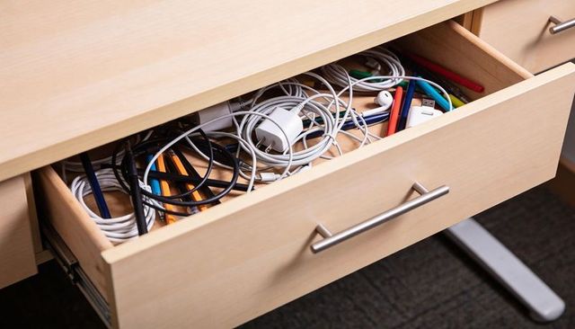 Tangled charging cables and chargers in light wood desk drawer showing office clutter