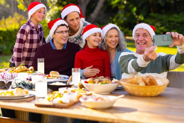 Caucasian parents, son, daughter and grandparents in santa hats taking selfie in garden, copy space. Family, christmas, celebration, togetherness and happiness concept.