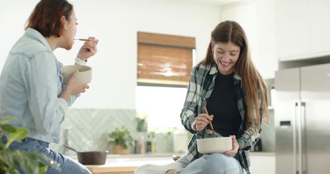 Diverse friends sharing casual breakfast on kitchen counter stirring bowls in bright modern kitchen