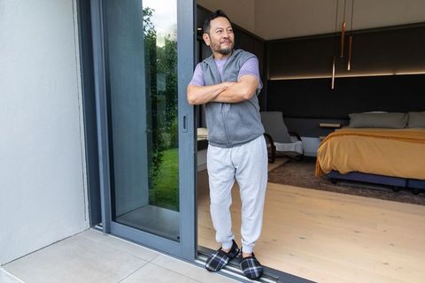 Mature asian man standing at sliding door in slippers and vest, enjoying quiet morning
