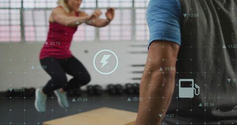 Trainer watching athlete jumping while man resting on plyo box with fitness tech overlay