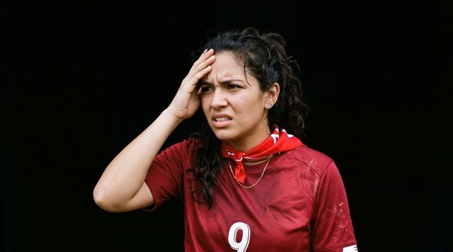 Tired soccer player holding head on sideline wearing maroon #9 jersey and red bandana