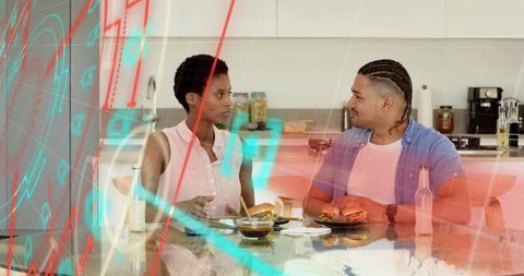 Couple chatting and eating burgers at modern glass dining table in contemporary kitchen