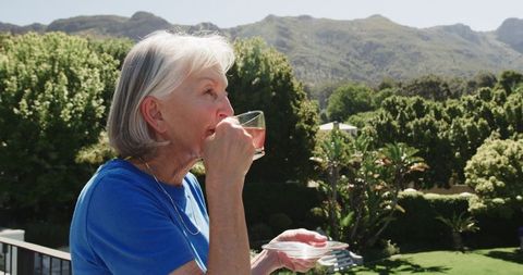 Senior Woman Enjoying Tea on Balcony Overlooking Scenic Garden