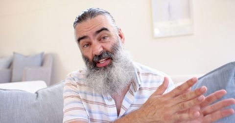 Elderly Man with Beard Gesturing in Conversation at Home