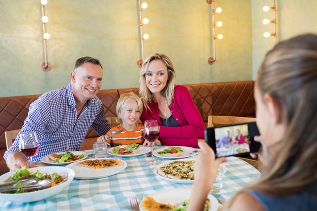 Girl photographing family through smart phone at restaurant