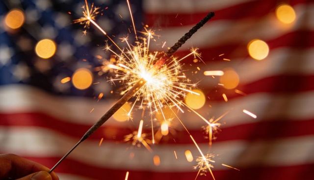 Holding sparkler celebrating fourth of july with american flag bokeh background