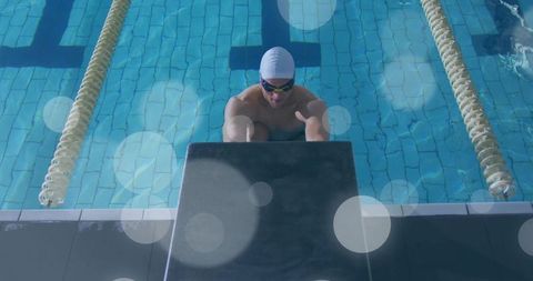 Competitive swimmer gripping starting block and holding lane rope at sunlit lap pool