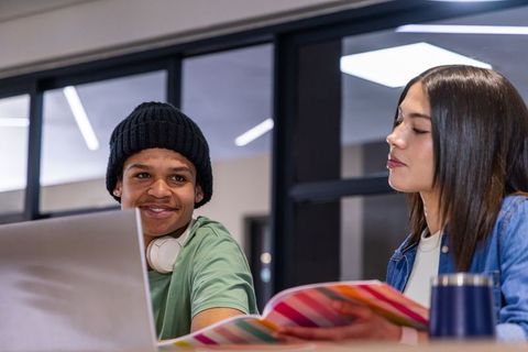 Teen students studying together in modern campus library with laptop and notebook
