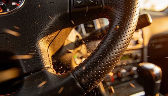 Perforated leather steering wheel with red stitching and sunlit dust particles