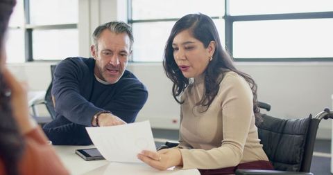 Inclusive team collaborating over document in modern office with woman using wheelchair