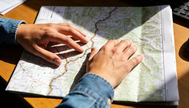 Planning road trip tracing route on folded topographic map with hands in denim sleeves